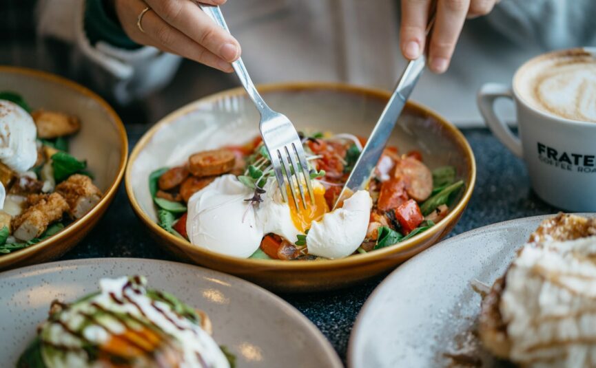 a close up of a lady eating brunch with 5 other meals on the table